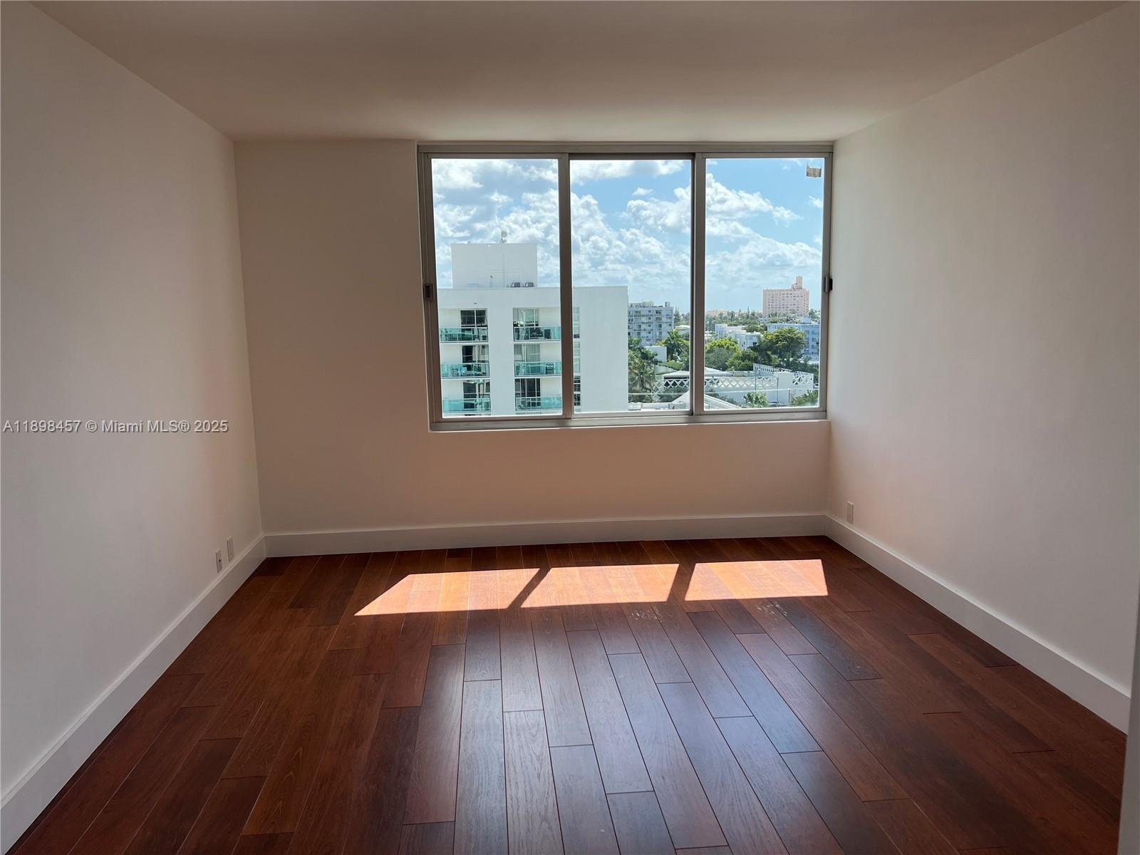 An empty room features dark wood flooring, white walls, and a large three-pane window — 1000 West Ave # 808, Miami Beach FL 33139, MIAMI BEACH, FL