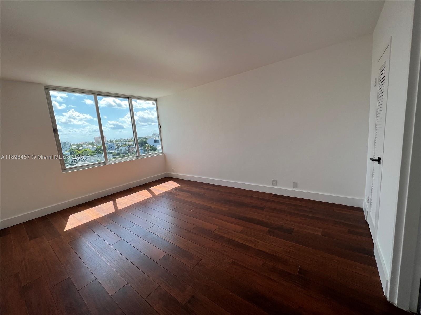 An empty bedroom features dark wood flooring, white walls, and a large window with city views — 1000 West Ave # 808, Miami Beach FL 33139, MIAMI BEACH, FL