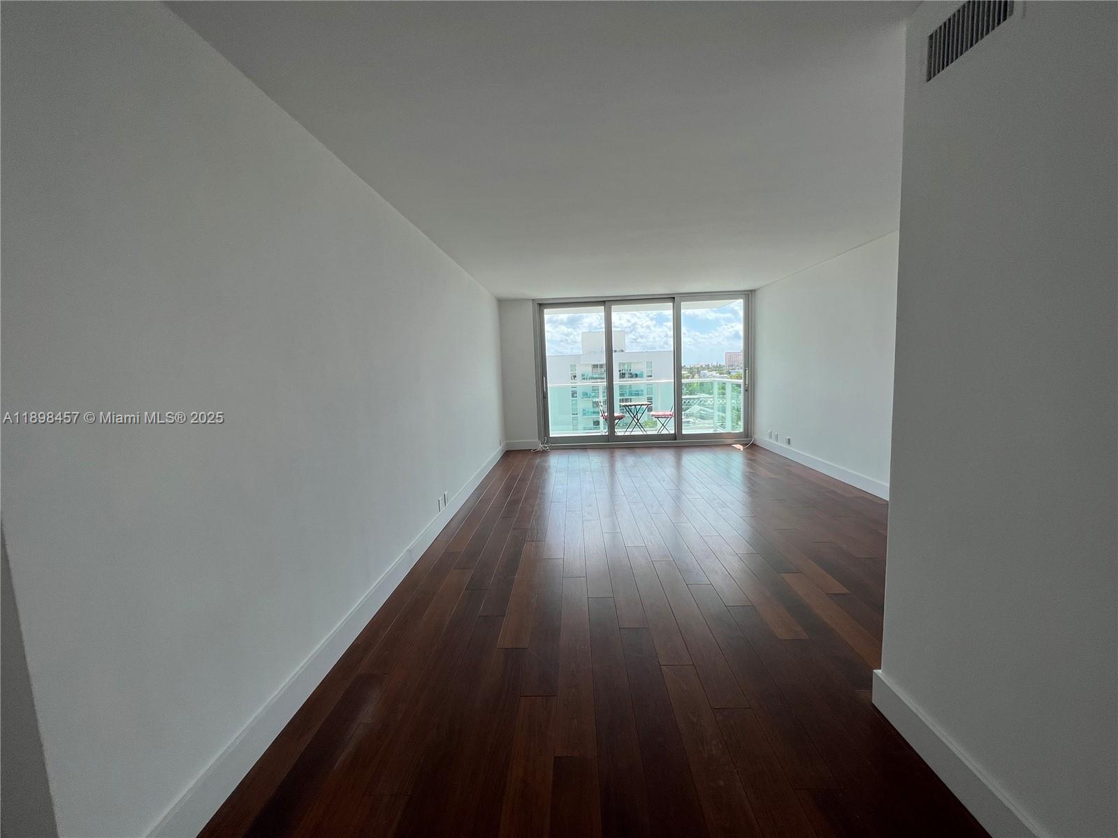 An empty room features dark wood flooring, white walls, and a glass sliding door balcony — 1000 West Ave # 808, Miami Beach FL 33139, MIAMI BEACH, FL