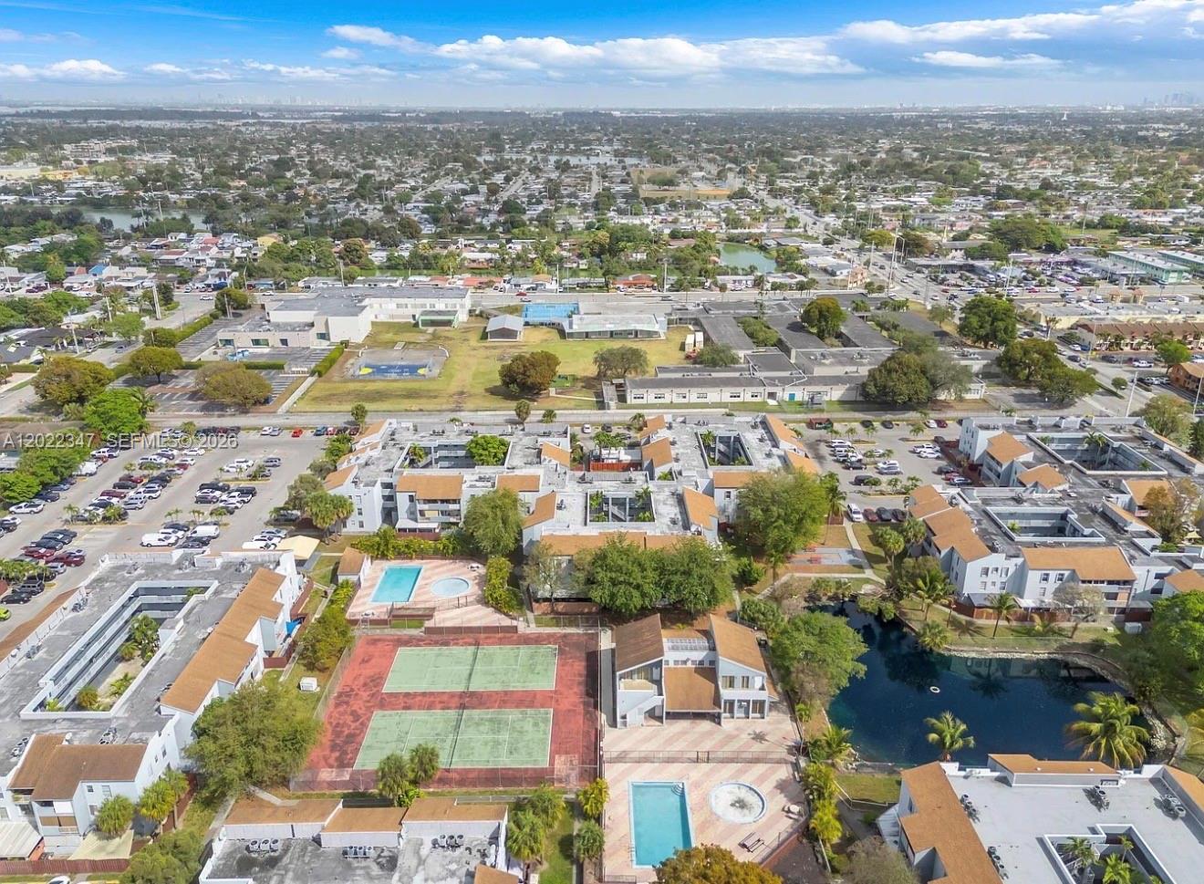 An aerial view of a residential complex featuring tennis courts, swimming pools, and a pond — 1725 W 60th St # F322, Hialeah FL 33012, HIALEAH, FL