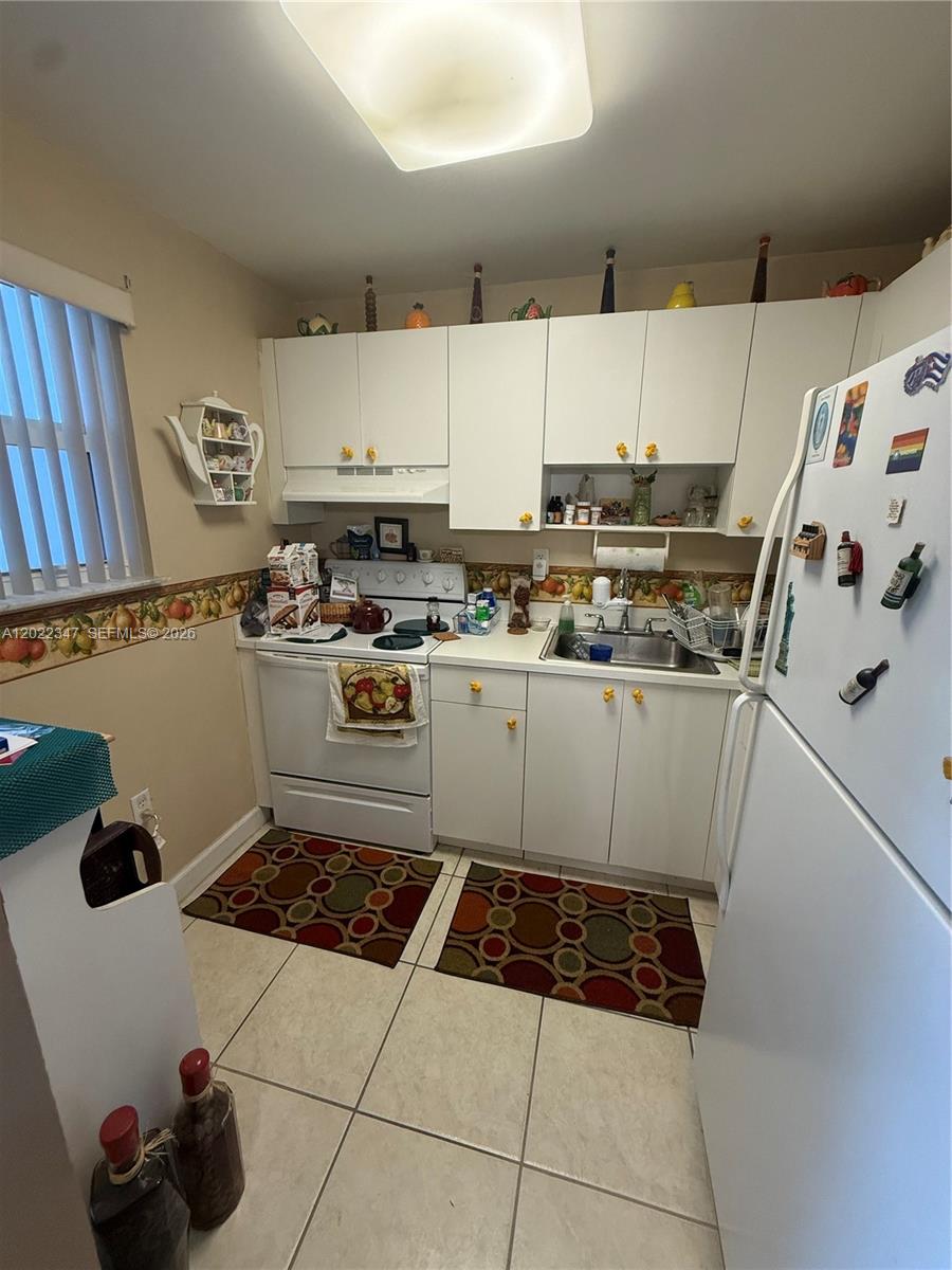 A small kitchen features white cabinets, white appliances, tiled floors, and a fruit-patterned wallpaper border — 1725 W 60th St # F322, Hialeah FL 33012, HIALEAH, FL