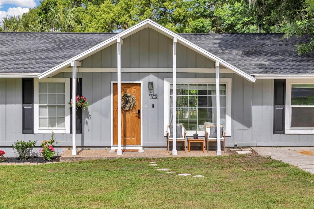 The exterior of a gray, single-story house features a wooden door and a covered porch — 1302 SE SANCHEZ AVENUE, OCALA, FL