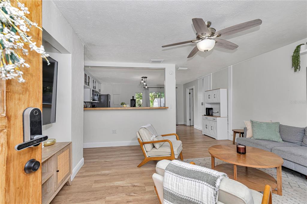 A living room with light wood flooring, a ceiling fan, and an open kitchen pass-through — 1302 SE SANCHEZ AVENUE, OCALA, FL