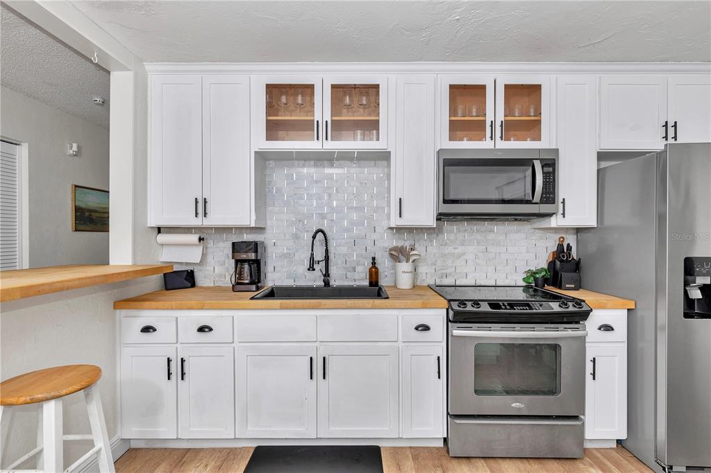 A kitchen features white cabinets, a butcher block countertop, a subway tile backsplash, and appliances — 1302 SE SANCHEZ AVENUE, OCALA, FL