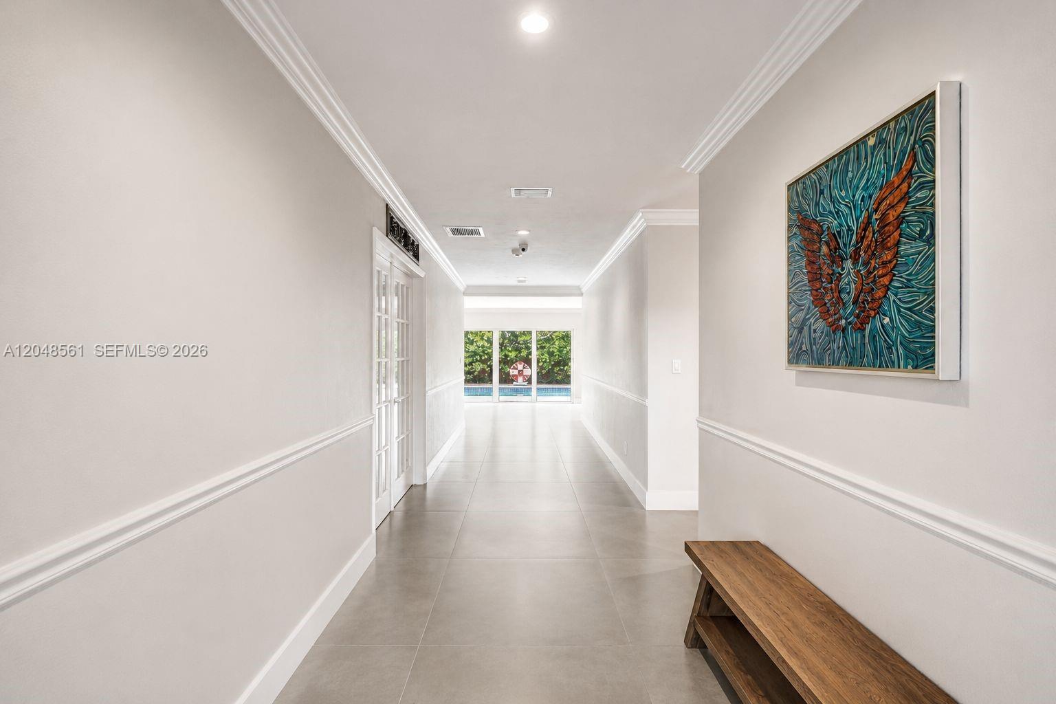 A long, tiled hallway features white walls, crown molding, a wooden bench, and wall art — 2220 NE 204th St, Miami FL 33180, MIAMI, FL