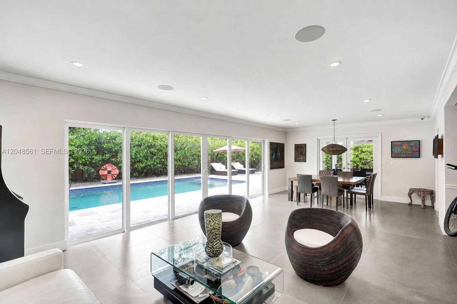 A bright living and dining area features large glass sliding doors overlooking a swimming pool — 2220 NE 204th St, Miami FL 33180, MIAMI, FL
