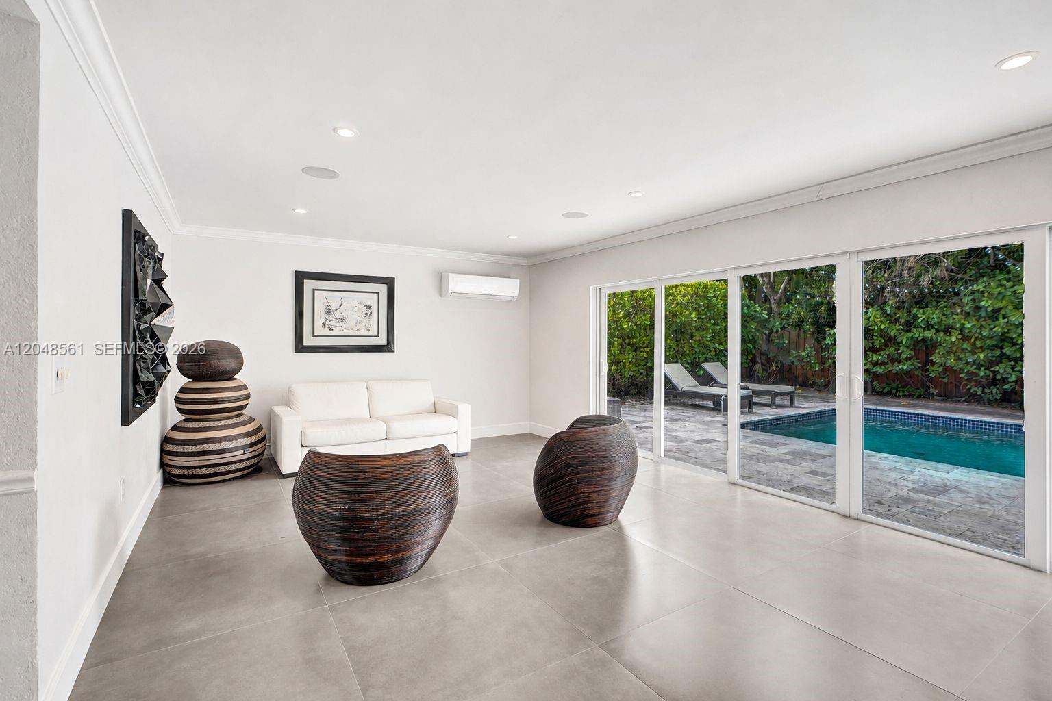 A living room features a white sofa, two dark rounded chairs, and sliding glass doors — 2220 NE 204th St, Miami FL 33180, MIAMI, FL