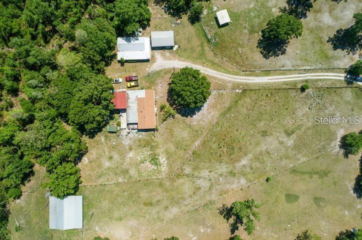An aerial view shows a rural property with a house, several outbuildings, and a dirt driveway — 6810 PEARSON LANE, WESLEY CHAPEL, FL
