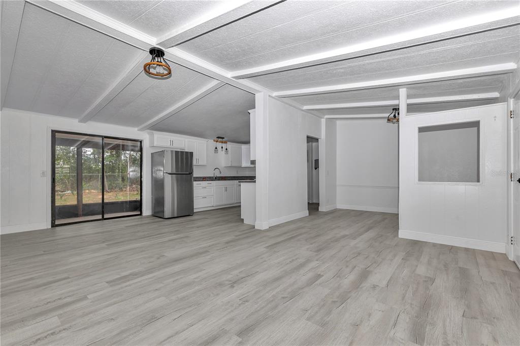 An open-concept living area with light wood-look flooring, white walls, and a kitchen — 6741 SW 84TH STREET, OCALA, FL