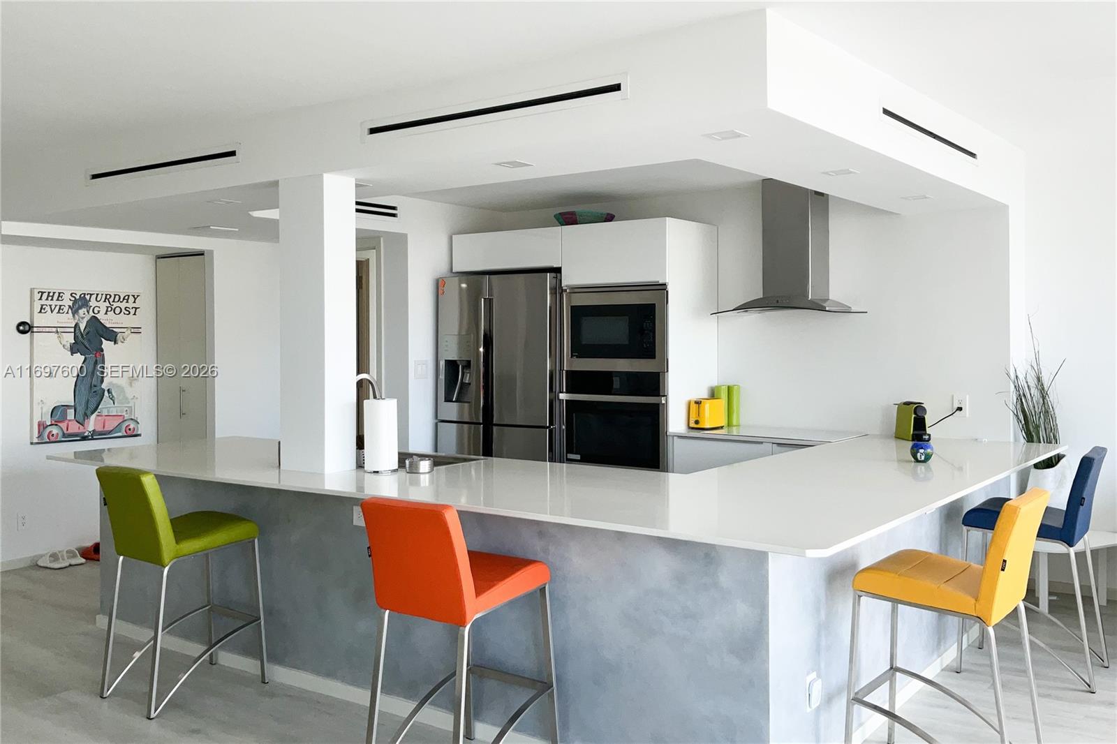 A modern kitchen features a white countertop island, colorful bar stools, and stainless steel appliances — 800 Parkview Dr # 708, Hallandale Beach FL 33009, HALLANDALE BEACH, FL
