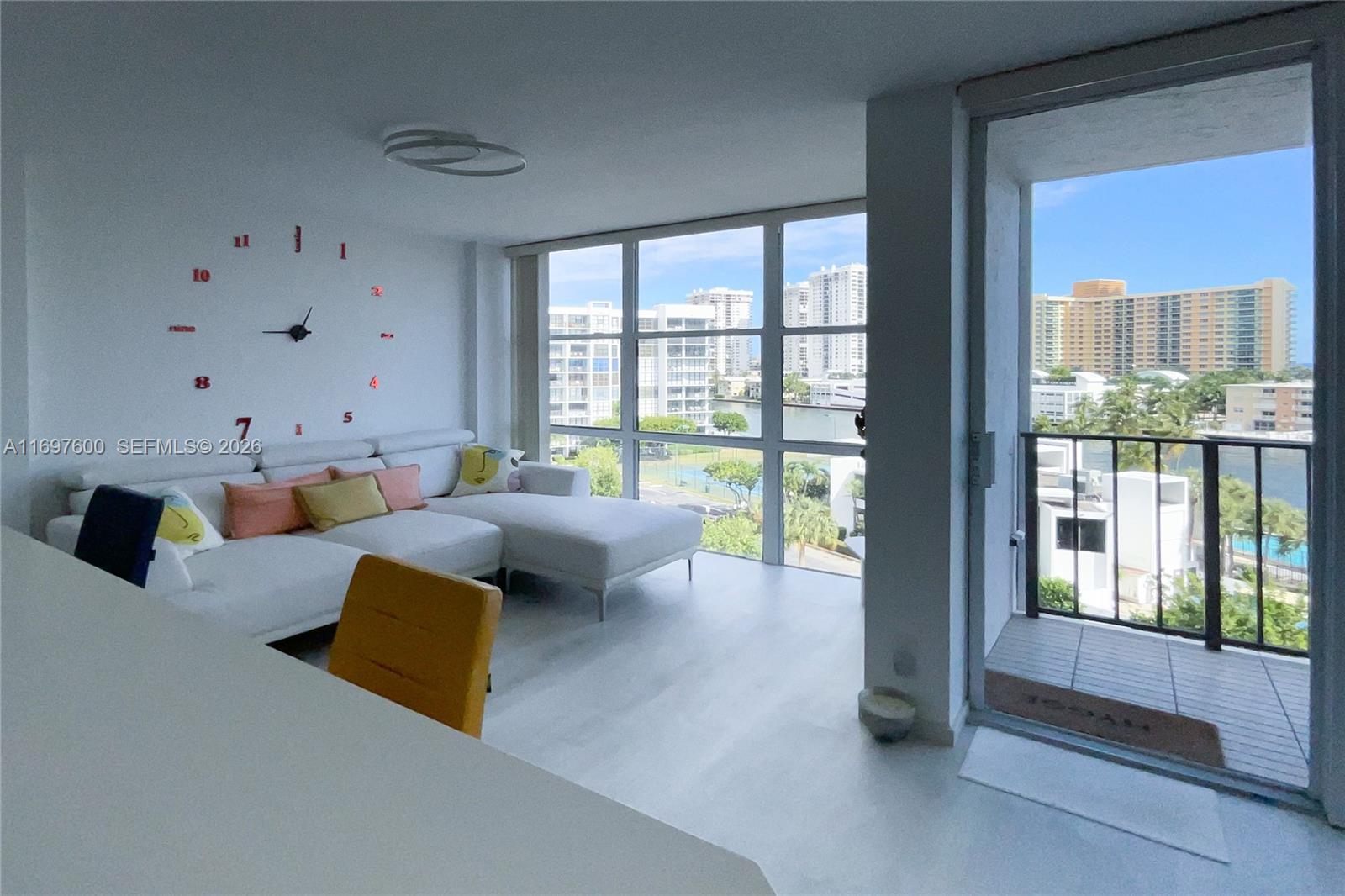 A living room features a white sectional sofa, a wall clock, and floor-to-ceiling windows — 800 Parkview Dr # 708, Hallandale Beach FL 33009, HALLANDALE BEACH, FL