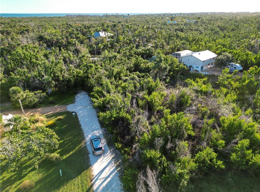 An aerial view shows a gravel driveway leading to a house surrounded by dense trees — 491 MARIAN ROAD, SANIBEL, FL