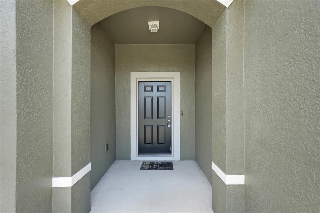 A dark front door with glass panels is centered within a covered entryway — 3923 WIND DANCER CIRCLE, ST CLOUD, FL