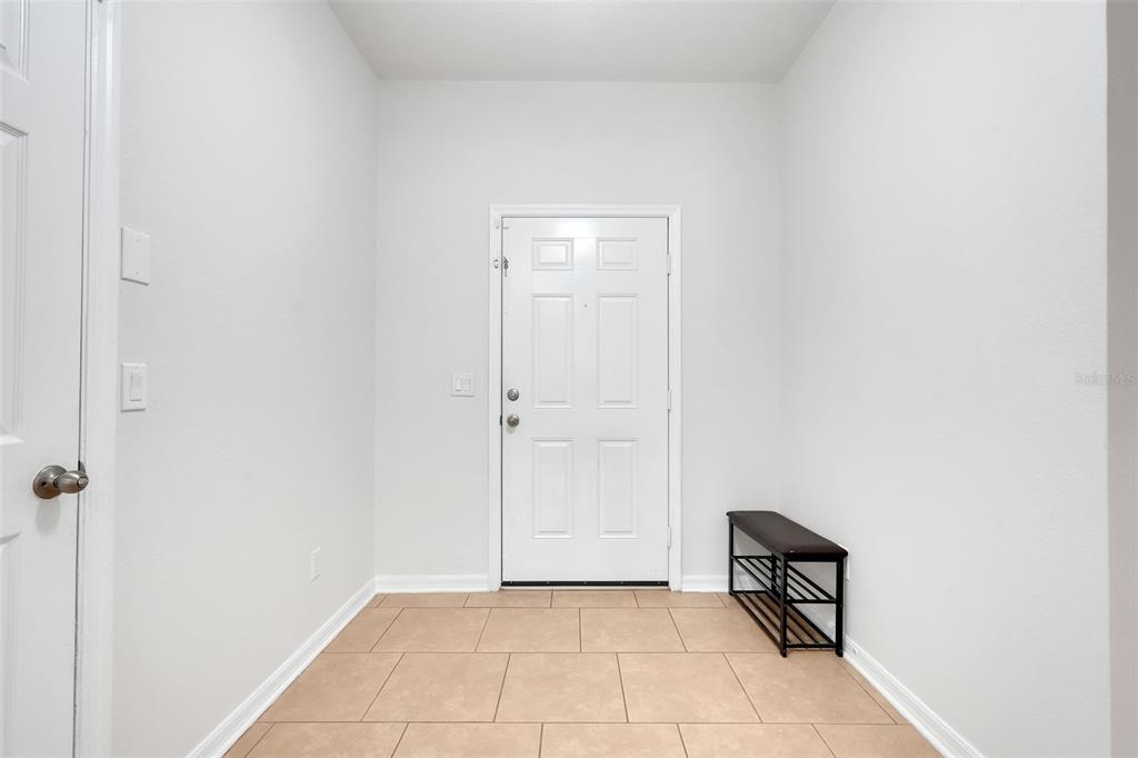 An entryway features white walls, tan tile flooring, a white front door, and a shoe rack — 3923 WIND DANCER CIRCLE, ST CLOUD, FL