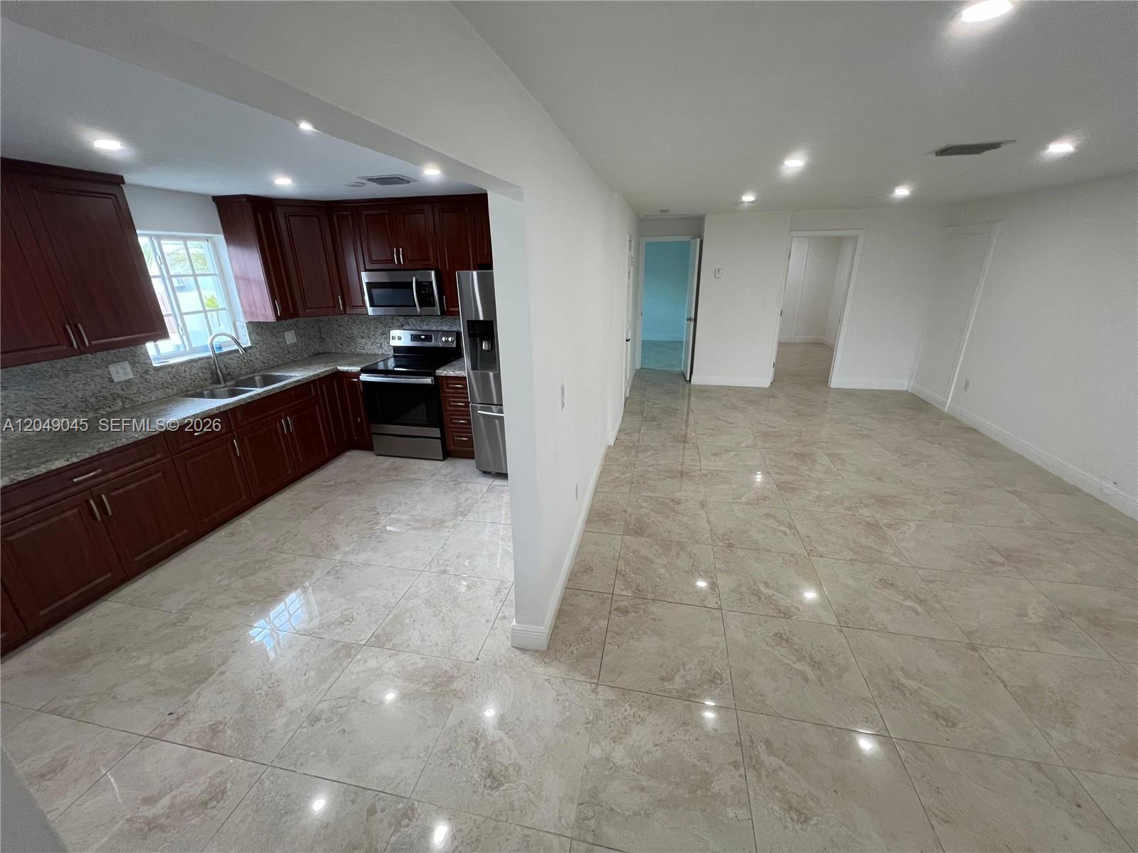 A kitchen with dark wood cabinets and granite countertops opens into a tiled living area — 4365 W 1st Ave # 1, Hialeah FL 33012, HIALEAH, FL