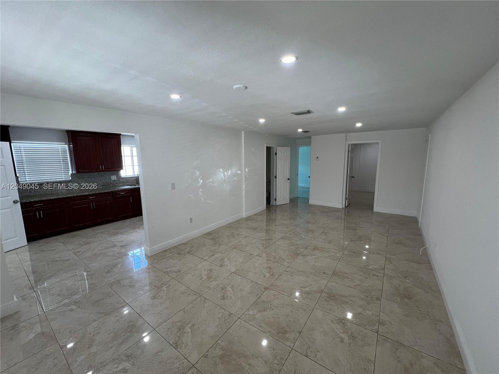 A living area with large beige floor tiles connects to a dark wood kitchen — 4365 W 1st Ave # 1, Hialeah FL 33012, HIALEAH, FL