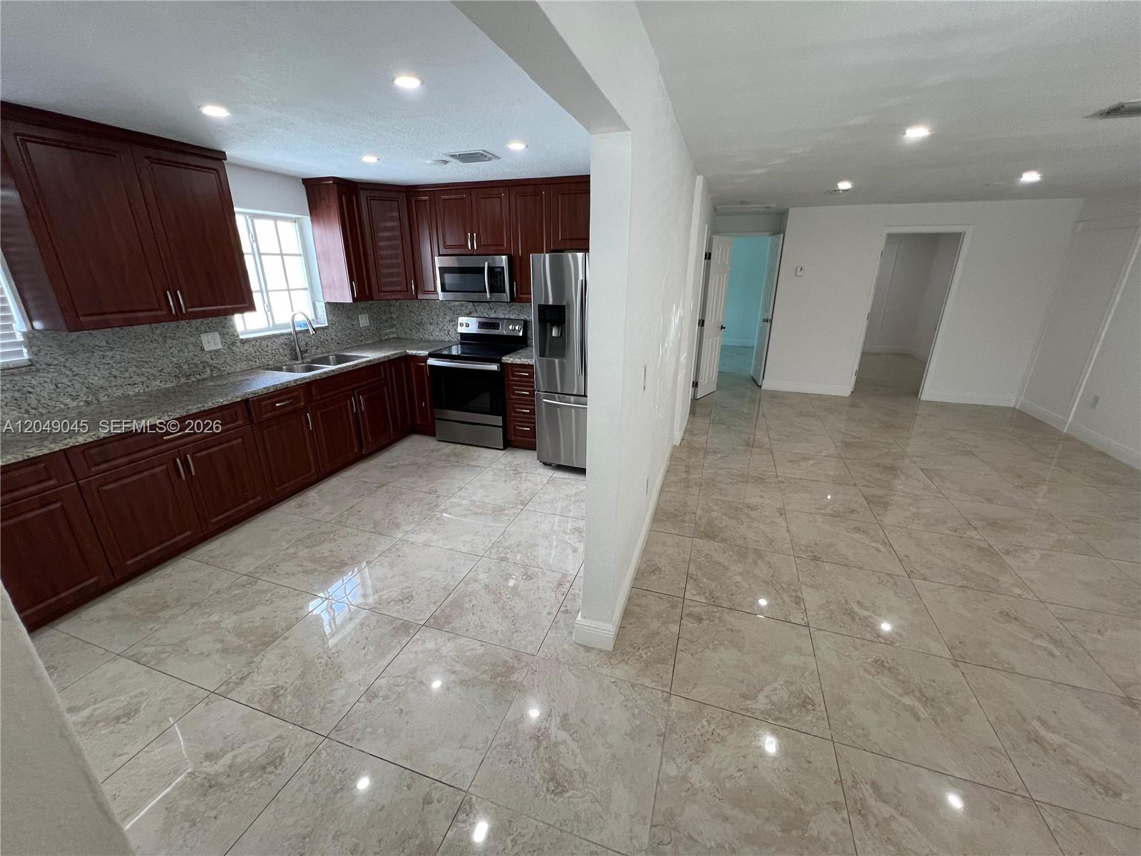 A kitchen with dark wood cabinets and granite countertops opens into a tiled living area — 4365 W 1st Ave # 1, Hialeah FL 33012, HIALEAH, FL