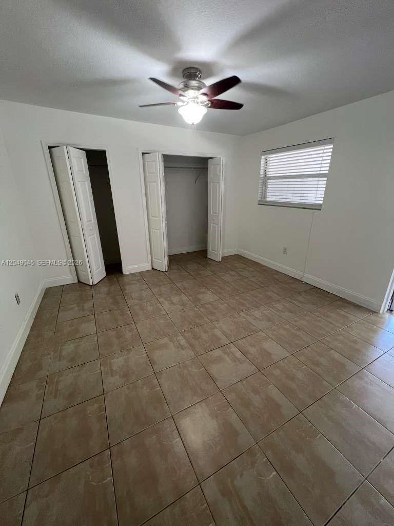 A bedroom with white walls, tile flooring, a ceiling fan, and two open closets — 4365 W 1st Ave # 1, Hialeah FL 33012, HIALEAH, FL