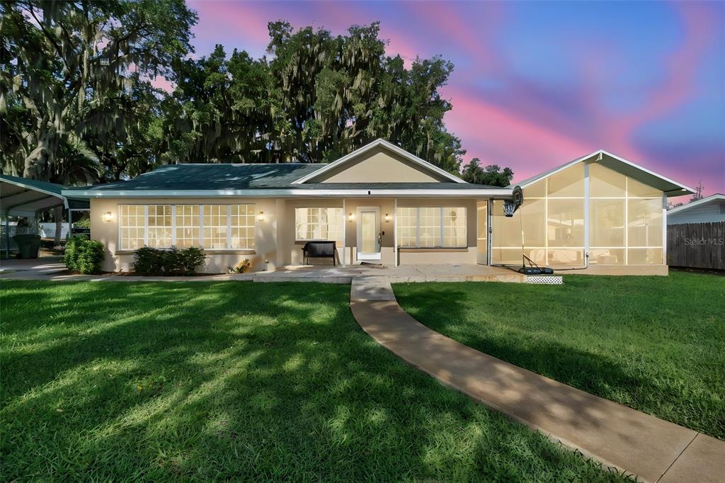 A single-story house with a screened-in porch, a concrete walkway, and large shade trees — 606 N SHORE DRIVE, LEESBURG, FL