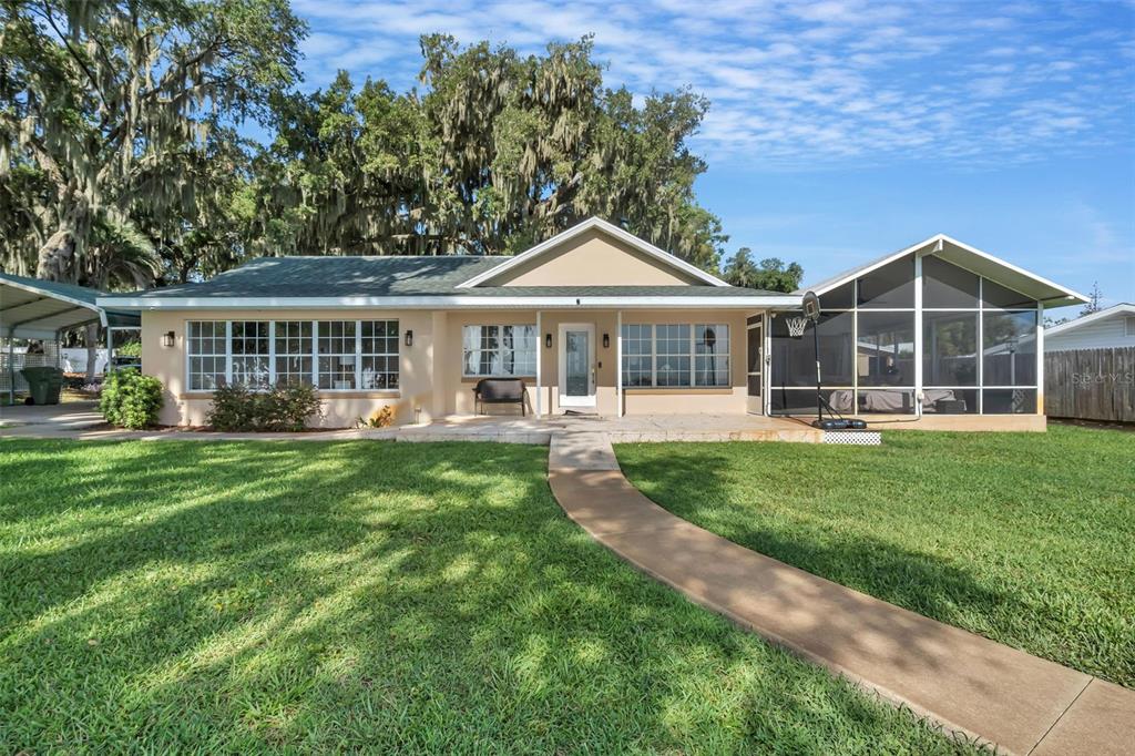 A single-story house with a screened-in porch, a concrete walkway, and large shade trees — 606 N SHORE DRIVE, LEESBURG, FL