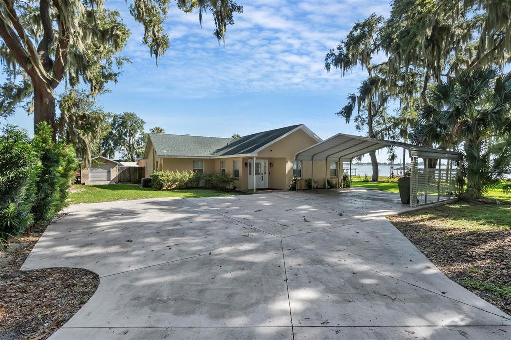 A single-story house with a concrete driveway and a metal carport under large trees — 606 N SHORE DRIVE, LEESBURG, FL