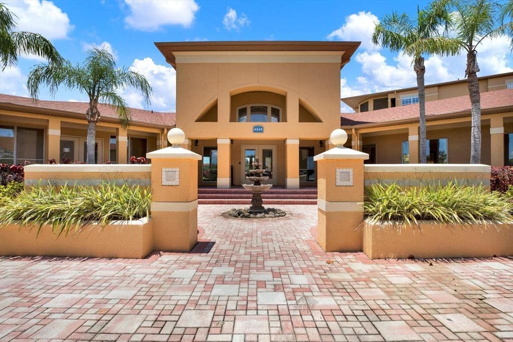 A paved walkway leads to the entrance of a tan building with a central fountain — 4333 BAYSIDE VILLAGE DRIVE UNIT 229, TAMPA, FL