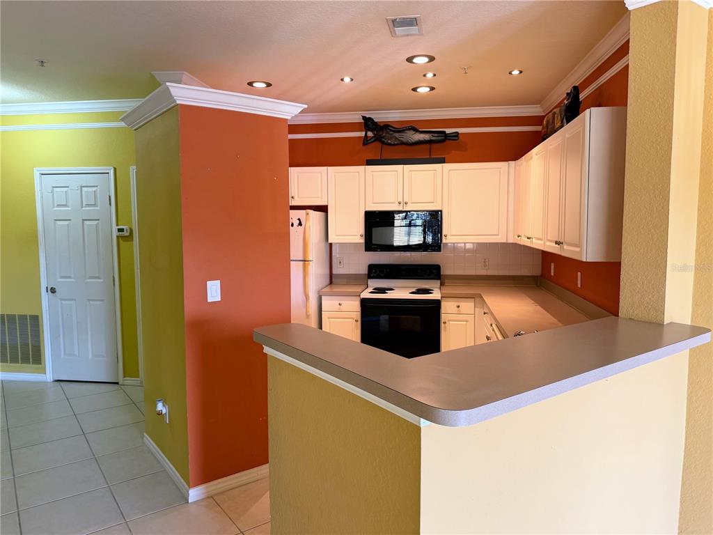 A kitchen features white cabinets, black appliances, and a breakfast bar with yellow and orange walls — 4333 BAYSIDE VILLAGE DRIVE UNIT 229, TAMPA, FL
