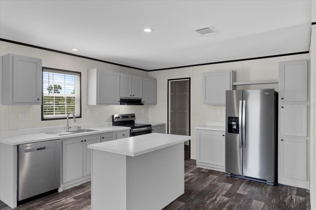 A kitchen features light gray cabinets, stainless steel appliances, a center island, and wood-look flooring — 21351 CANAL DRIVE, BROOKSVILLE, FL