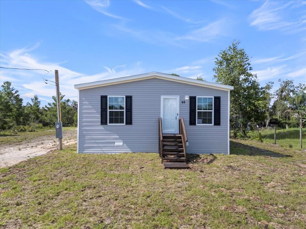 A single-story gray manufactured home with black shutters stands on a grassy lot — 21351 CANAL DRIVE, BROOKSVILLE, FL