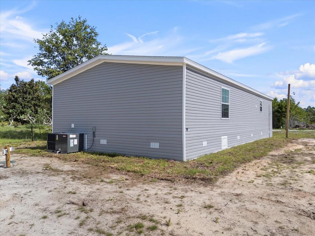 The exterior of a gray vinyl-sided manufactured home sits on a sandy, undeveloped lot — 21351 CANAL DRIVE, BROOKSVILLE, FL