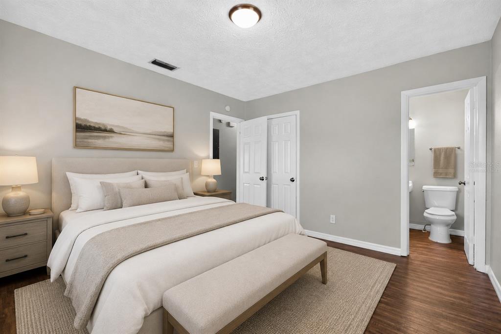 A bedroom with a bed, bench, nightstands, and an attached bathroom with wood-look flooring — 3734 BARMER DRIVE, JACKSONVILLE, FL
