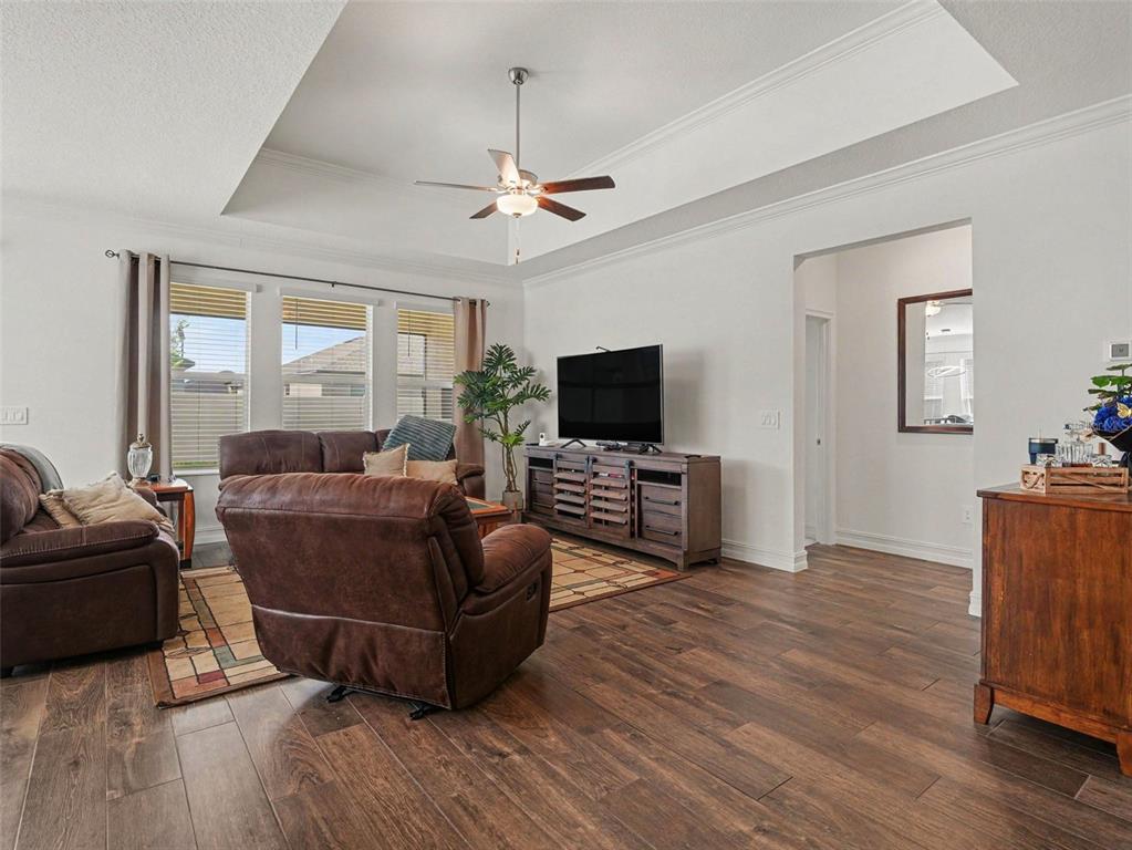 A living room features wood-look tile flooring, a tray ceiling with a fan, and brown furniture — 11704 74TH CIR E, PALMETTO, FL