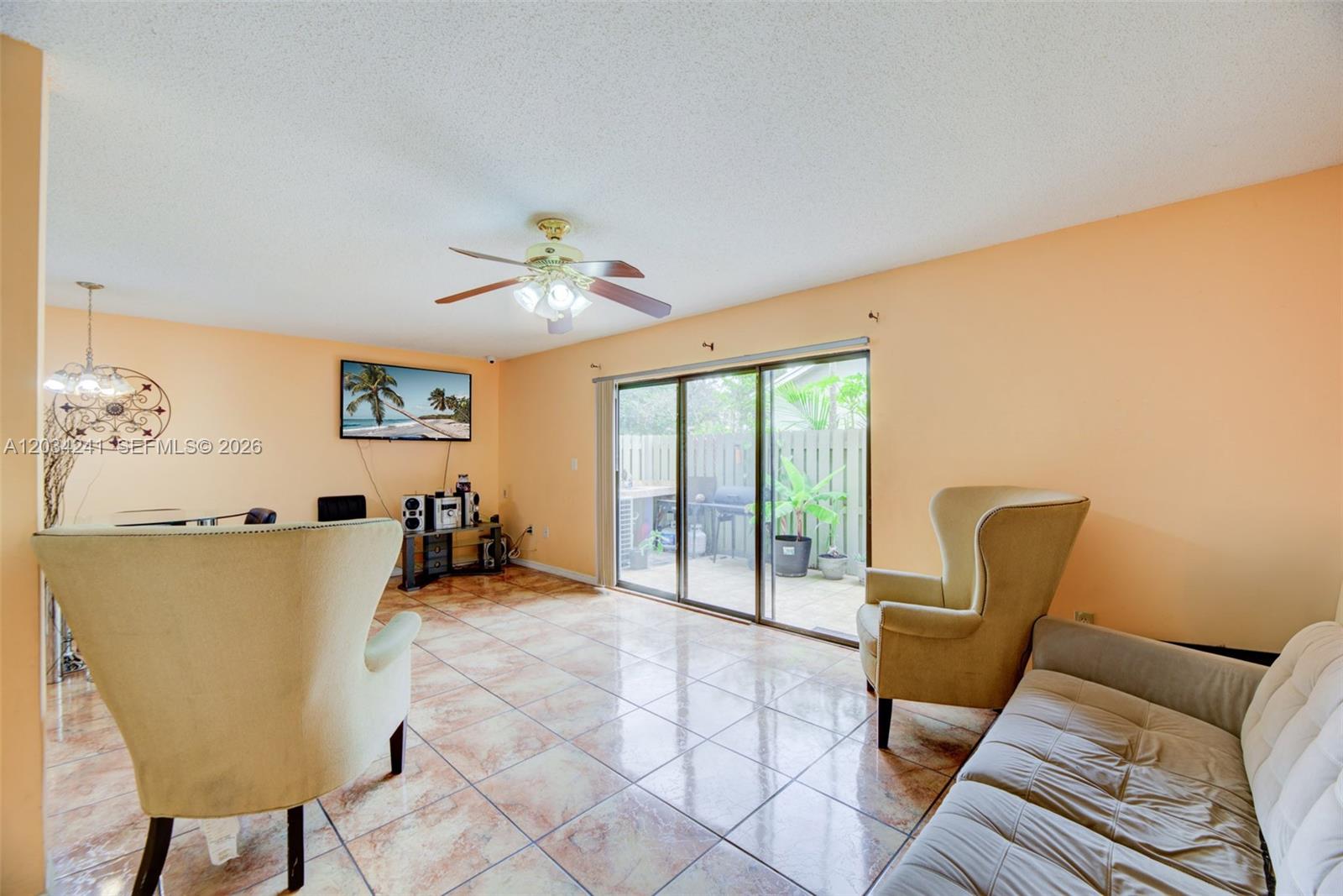 A living room features peach walls, tile flooring, a ceiling fan, and sliding glass doors — 7661 NW 38th Ct, Sunrise FL 33351, SUNRISE, FL