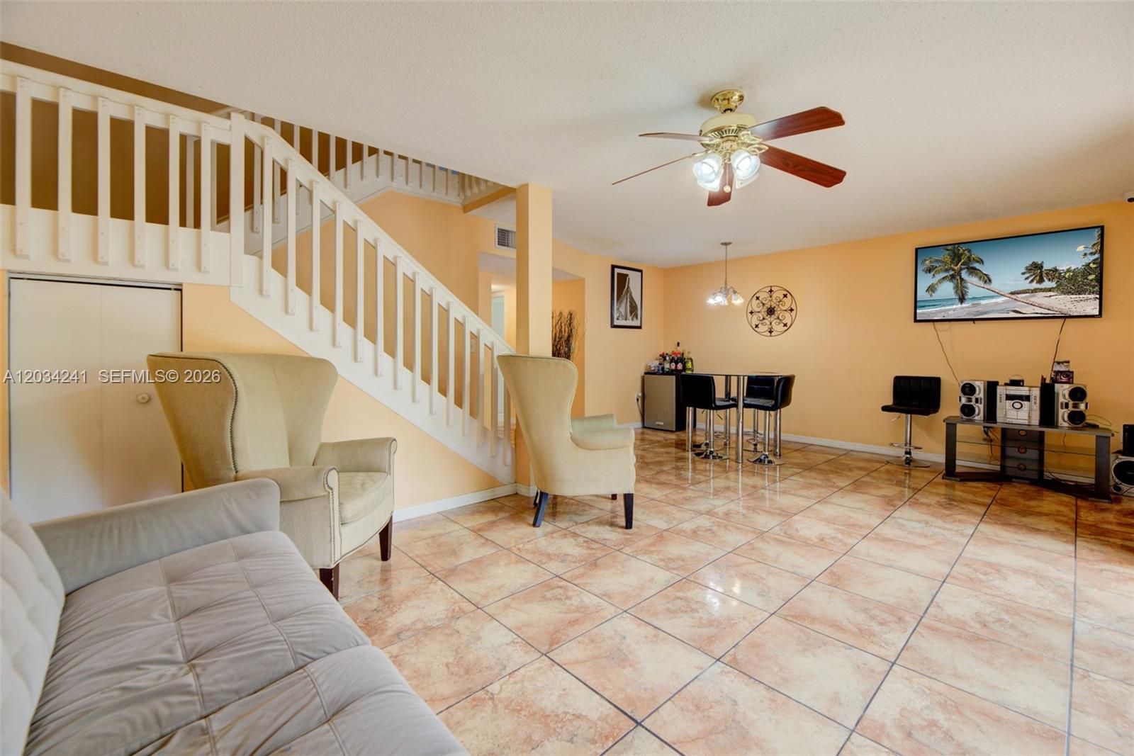 A living room features tile flooring, a staircase, beige armchairs, and a wall-mounted television — 7661 NW 38th Ct, Sunrise FL 33351, SUNRISE, FL