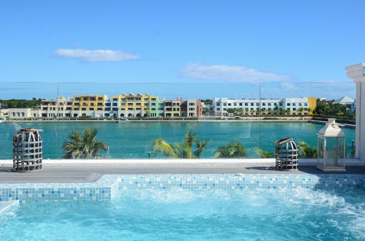 A swimming pool overlooks a body of water with a row of colorful buildings beyond — . Condominio Fundadores Marina Cap Cana, FL, FL