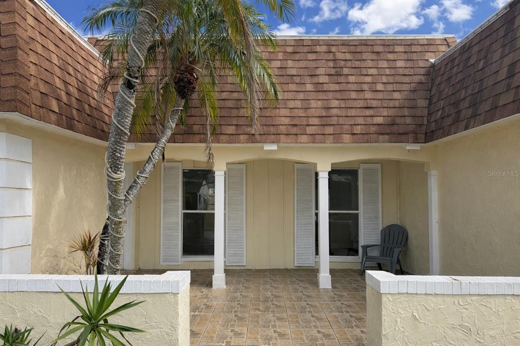 A covered patio with tiled flooring sits in front of a house with light-colored walls — 3628 LANDALE DRIVE, HOLIDAY, FL