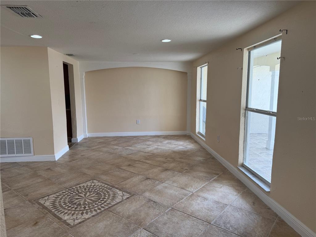 An empty room features beige walls, tile flooring with a decorative inlay, and two windows — 3628 LANDALE DRIVE, HOLIDAY, FL