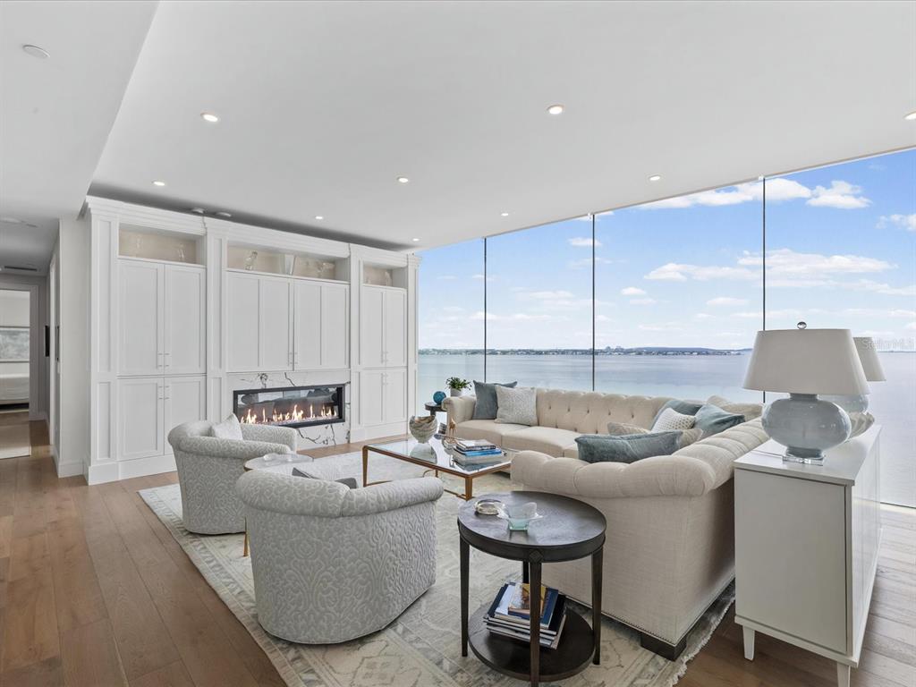 A modern living room features a fireplace, built-in cabinetry, and floor-to-ceiling windows overlooking the water — 2619 BAYSHORE BOULEVARD UNIT 900, TAMPA, FL