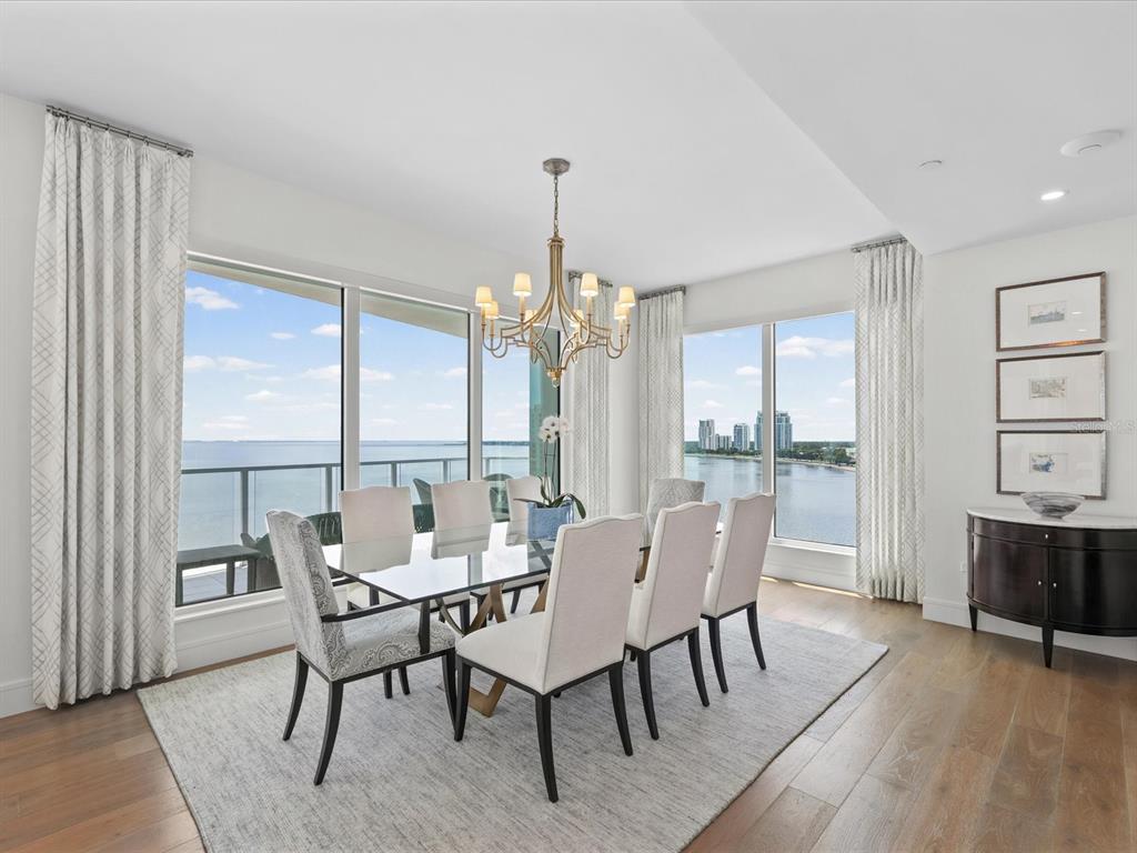 A dining room features a glass table, upholstered chairs, a chandelier, and floor-to-ceiling water views — 2619 BAYSHORE BOULEVARD UNIT 900, TAMPA, FL