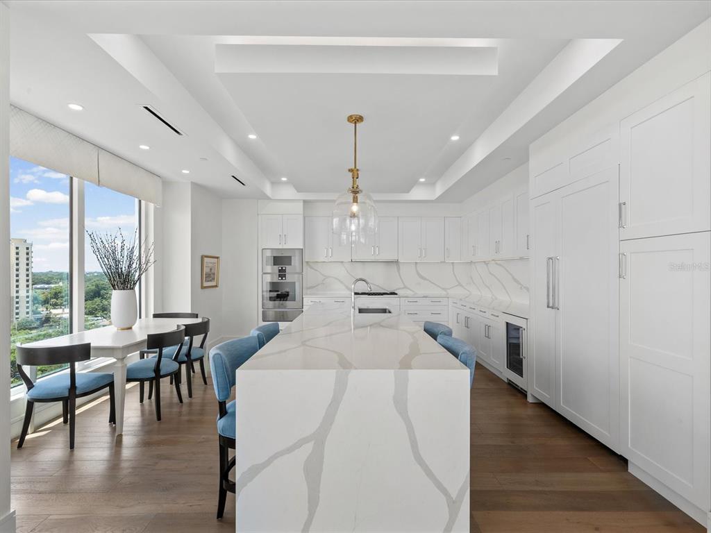 A modern white kitchen features a large marble waterfall island, blue chairs, and floor-to-ceiling windows — 2619 BAYSHORE BOULEVARD UNIT 900, TAMPA, FL
