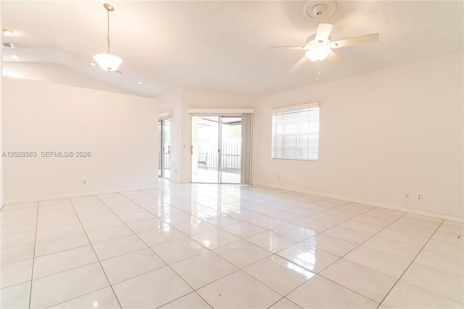 A bright, empty room features white tiled floors, a ceiling fan, and sliding glass doors — 1341 Seagrape Cir, Weston FL 33326, WESTON, FL