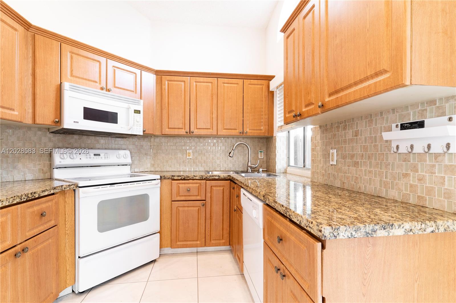 A kitchen features light wood cabinets, granite countertops, a white stove, and a tiled backsplash — 1341 Seagrape Cir, Weston FL 33326, WESTON, FL