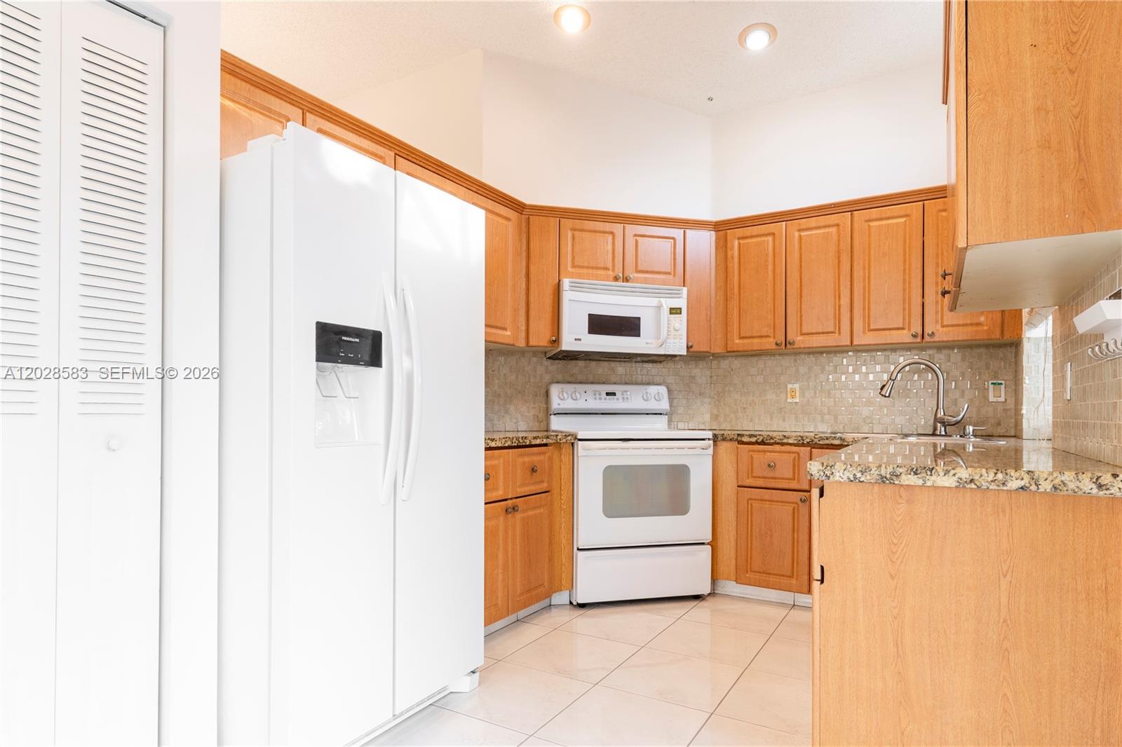 A kitchen features light wood cabinets, white appliances, granite countertops, and a tiled backsplash — 1341 Seagrape Cir, Weston FL 33326, WESTON, FL