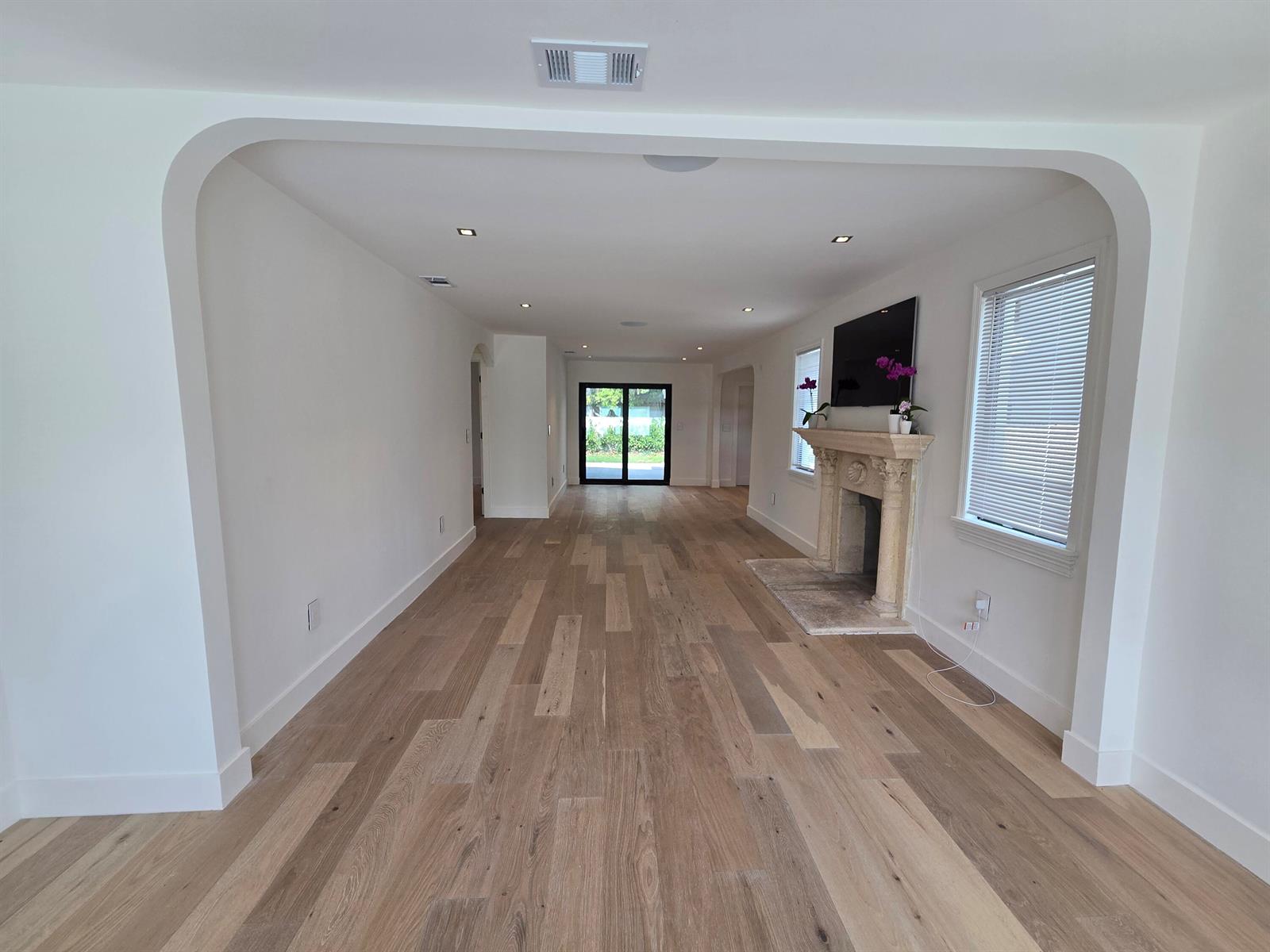An empty living room features light wood flooring, a stone fireplace, and an arched entryway — 3809 S Olive Avenue, West Palm Beach FL 33405, WEST PALM BEACH, FL