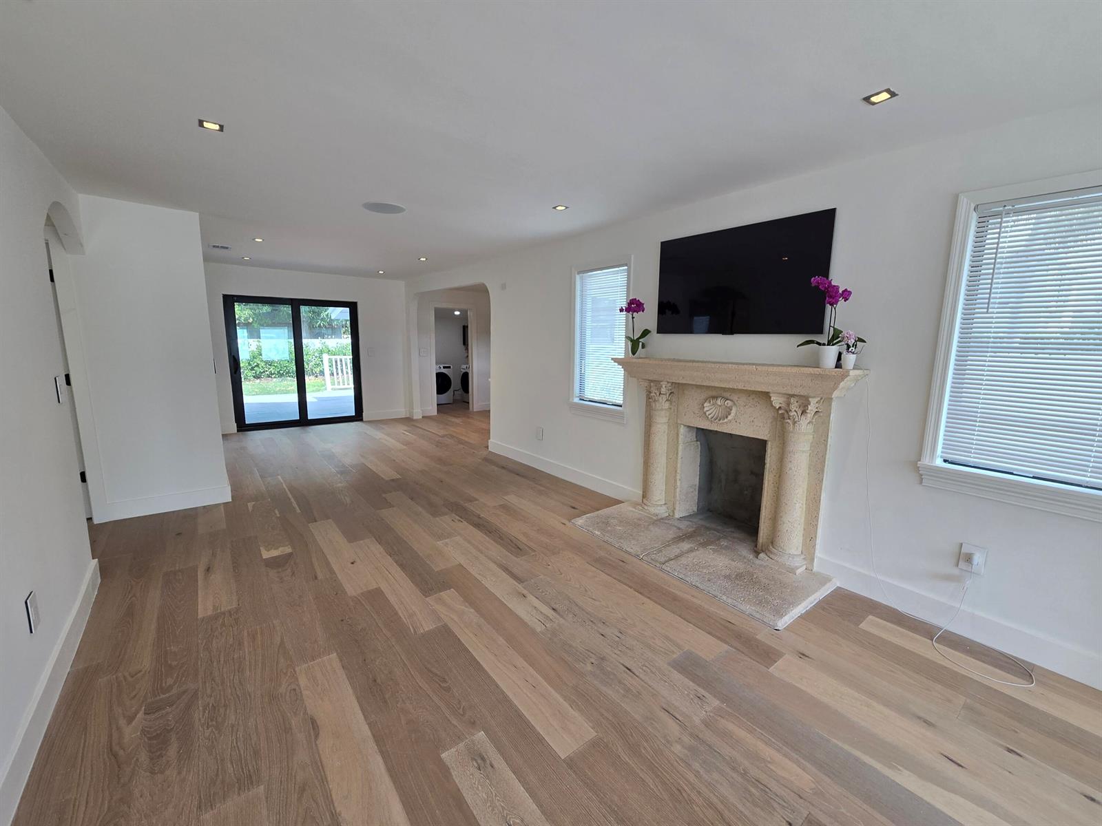 A living room features light wood flooring, a stone fireplace, and a wall-mounted television — 3809 S Olive Avenue, West Palm Beach FL 33405, WEST PALM BEACH, FL
