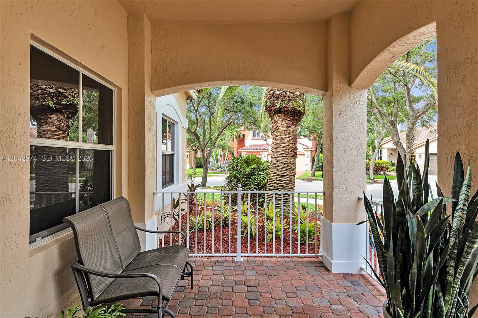 A covered patio features a brick floor, a metal bench, and a white railing — 3711 Falcon Ridge Cir, Weston FL 33331, WESTON, FL