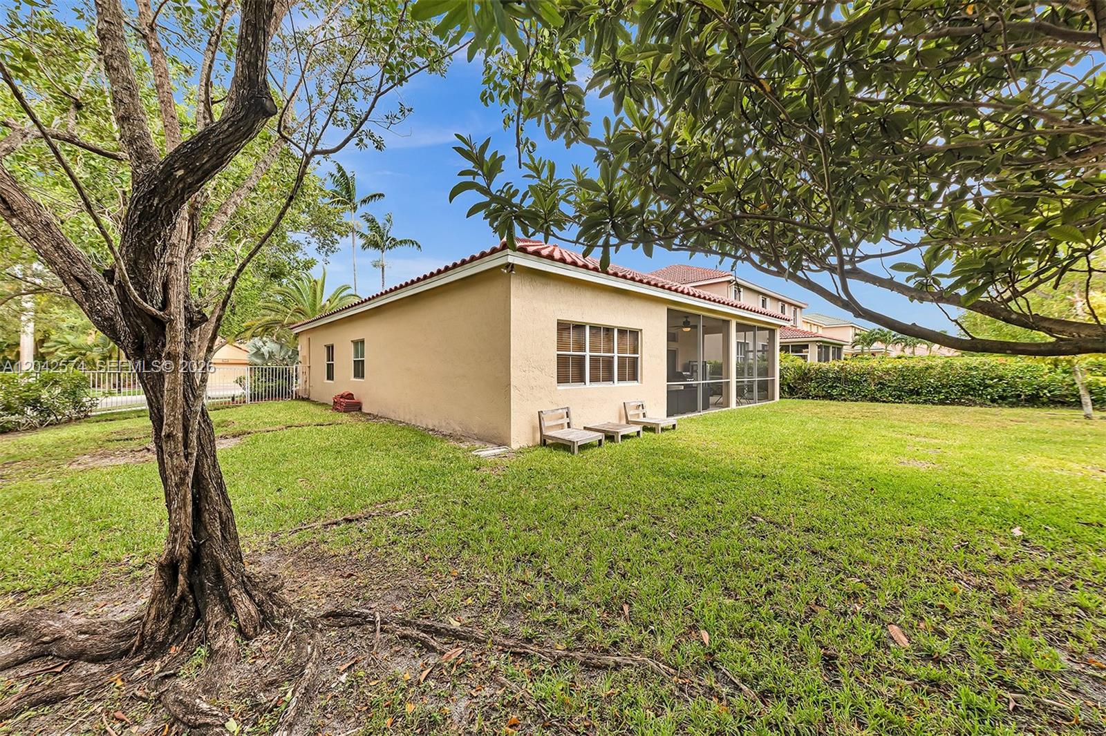 The exterior of a tan stucco house features a screened-in patio and a grassy backyard — 3711 Falcon Ridge Cir, Weston FL 33331, WESTON, FL