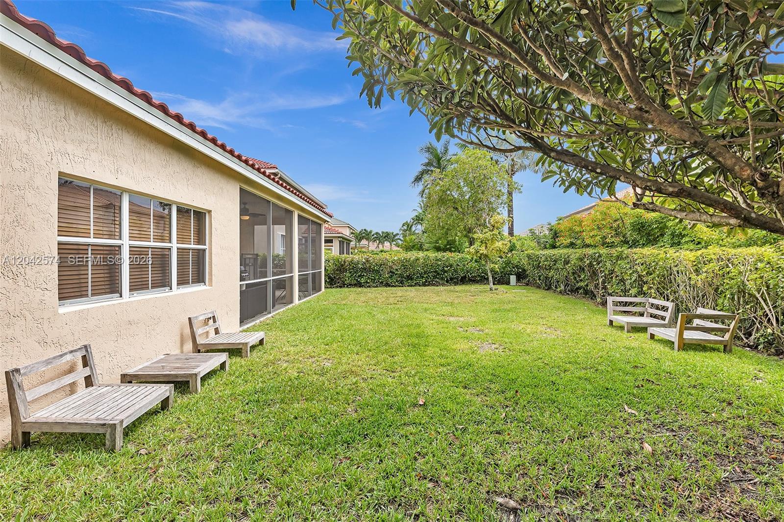 A grassy backyard features wooden benches along the side of a house with a screened-in porch — 3711 Falcon Ridge Cir, Weston FL 33331, WESTON, FL