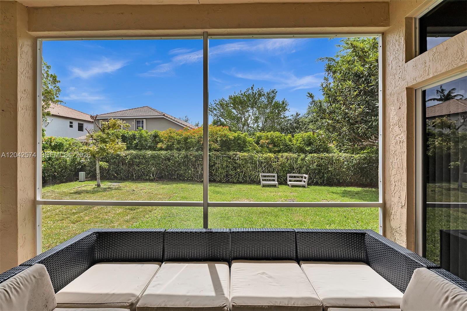 A screened-in patio features a wicker sofa overlooking a grassy backyard with a hedge — 3711 Falcon Ridge Cir, Weston FL 33331, WESTON, FL