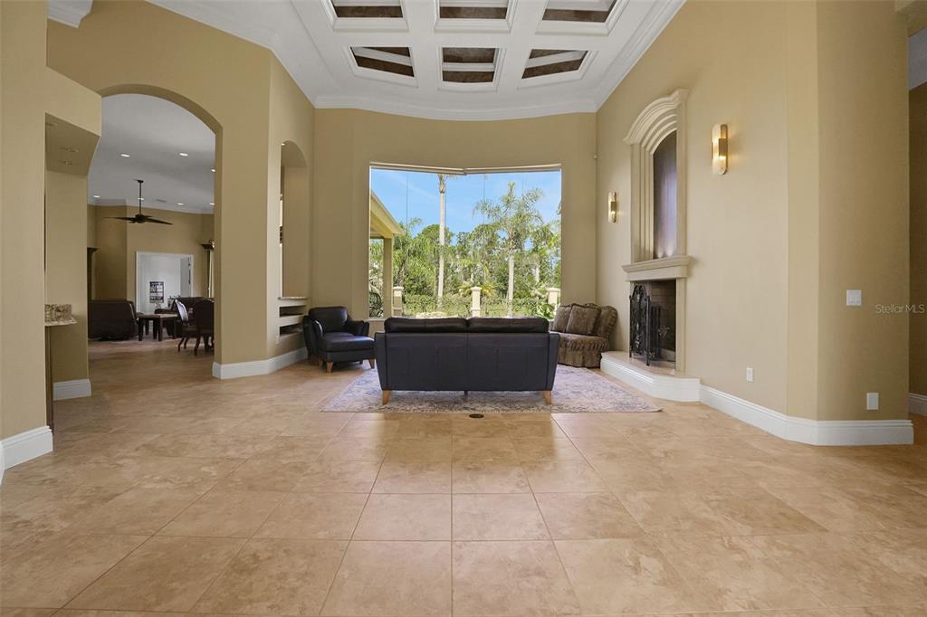 A spacious living room features tile flooring, a coffered ceiling, a fireplace, and large windows — 260 SPRING FOREST DRIVE, NEW SMYRNA BEACH, FL